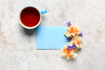 Cup of tea, beautiful flowers and blank card on light background