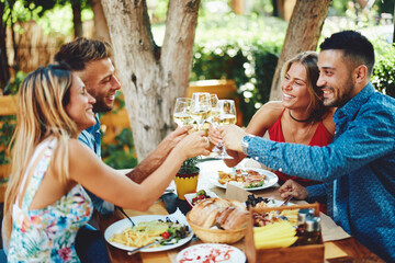 Group of young happy people toast with wine at lunch in restaurant during a sunny summer day - 440557765