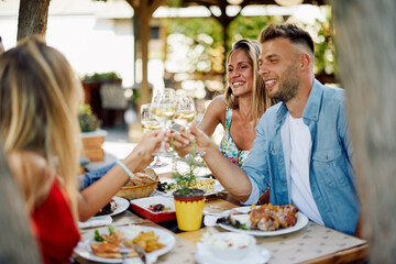 Group of young happy people toast with wine at lunch in restaurant during a sunny summer day