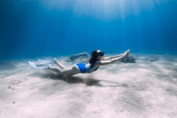 Female freediver dive with fins underwater in ocean with sunlight.