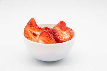Sliced ​​strawberries in a white plate against white background.