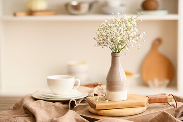 Vase with beautiful gypsophila flowers and cup of coffee on wooden table in kitchen