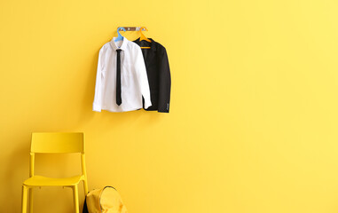 Hanger with stylish school uniform on color wall in room