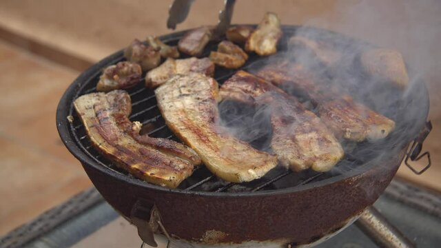 Parrillada de carne de cerdo  en la barbacoa port&aacute;til de panceta y morro, mano volteando la carne para que se ase por las dos caras