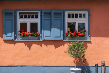 View of an orange house wall with two windows and blue shutters 