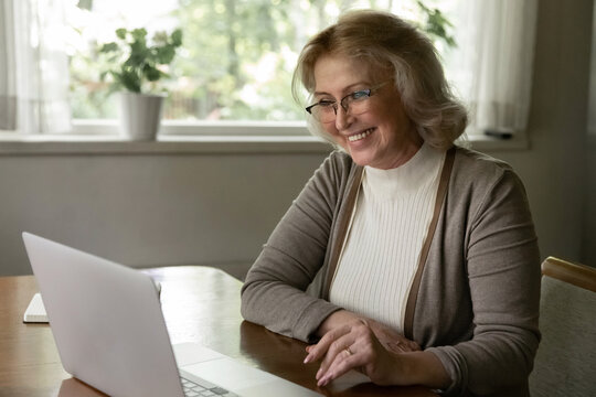 Happy senior Caucasian woman look at laptop screen talk speak on video call on device from home. Smiling old female use computer have webcam digital virtual event. Communication, technology concept.