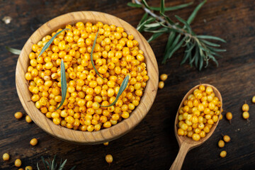Sea buckthorn. Fresh ripe berry in wooden bowl and a spoon with leaves on wood background.