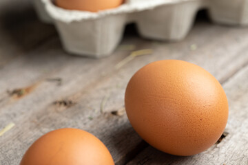 Brown eggs in a cardboard box. Eggs are scattered over a wooden background. Healthy food concept.