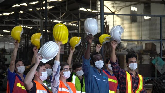 group of factory workers wear protective face mask excited and celebrating holding headhat rising up in meeting at industrial factory protect for pollution and coronavirus  or covid 19 pandemic