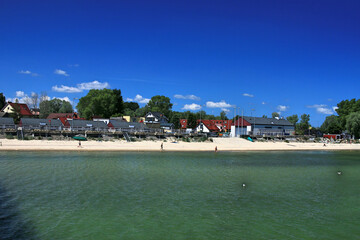 The Baltic Sea, the coast and the beach in Mechelinki in Poland. The Baltic Sea in summer. Blue sky, gulls floating on the water. People are sunbathing on the beach