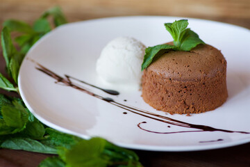 A cupcake or pancake with chocolate filling lies on a plate of ice cream. The dish is decorated for serving