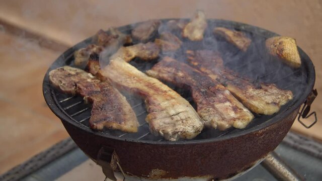 Parrillada de carne de cerdo  en la barbacoa port&aacute;til de panceta y morro, mano volteando la carne para que se ase por las dos caras