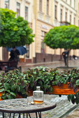 Fototapeta premium Bottle of alcohol near a glass on an empty table. The concept of alcoholism, loneliness and depression. Old vintage bottle on a wooden table. The table is wet from the rain.