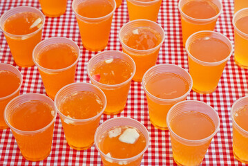 Fresh fruit punch on the table. Yellow drink in plastic cups. Summer drink on a checkered tablecloth.