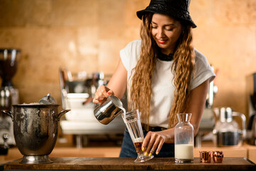 beautiful young woman barista pouring whipped cream into transparent glass with syrup
