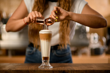 glass with syrup and whipped cream into which barista pours espresso from cups