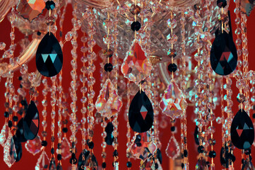 A fragment of a crystal chandelier on a red background with a noisy texture, with crystals of different shapes and sizes, close-up.
