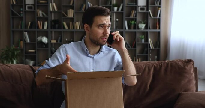 Man sitting on sofa with opened parcel express complaints to seller or courier on the phone about damaged goods, crashed items inside cardboard box. Dissatisfied e-commerce customer, claims concept