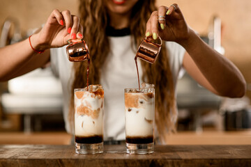 process of making macchiato with syrup. Woman carefully pours coffee from cups into glasses