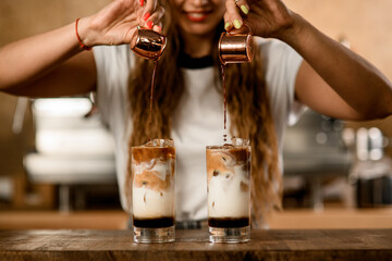 process of making cold coffee cocktail. Woman carefully pours espresso from cups into glasses