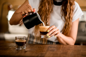 close-up on glass with coffee drink in which woman barista pours whipped milk cream