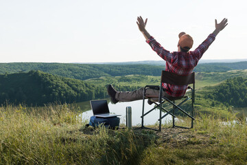 Fototapeta premium Man emotional happy raised hands enjoying nature. Remote work concept -happy adult man with laptop on top of mountain.