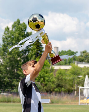 Happy Boy Child Soccer Player Champion In Children's Football Championship With Trophy Gold Cup With Golden Football Ball. Soccer Tournament. Kids Sport, Victory, Winner, Award Ceremony