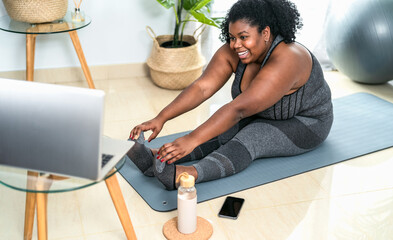 Young African curvy woman doing pilates online fitness class with laptop at home - Sport wellness...