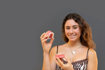 Portrait of smiling girl holding a denture with gray background.