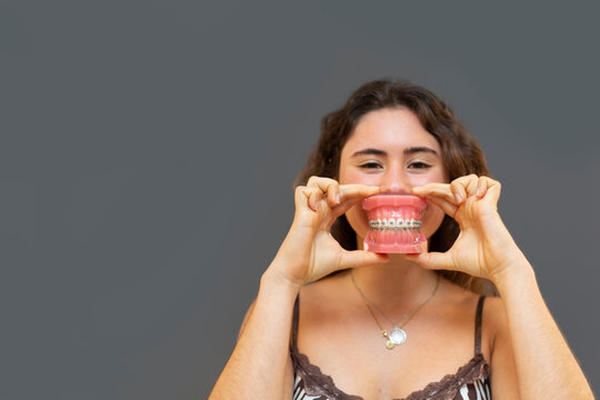 Portrait of smiling girl holding a denture with gray background.