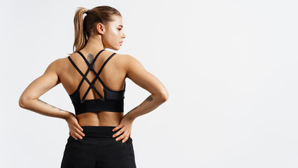Portrait of female athlete doing workout. Woman in fitness wear with hands on waist on white background. Rear view of athletic sportswoman muscular back in sportsbra