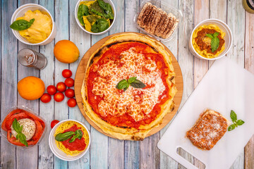 Top view image of typical Italian dishes with lots of basil, margarita pizza, tiramisu, bolognese noodles, cherry tomatoes, spaghetti, burrata