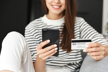 Cropped shot of young smiling woman, hands holding smartphone and credit card, concept of online shopping, internet purchase, paying with mobile phone