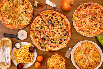 Top view image of typical Italian dishes, assorted sliced pizzas, potatoes, onions, cutlery and tomatoes with salt and pepper