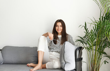 Portrait of young woman sit comfortable on living room sofa, smiling and watching smth with pleased, relaxed smile, resting at home on weekend