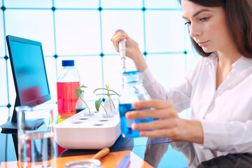 Young woman with a pipette in a plant laboratory. Study of the effect of growth accelerators on...