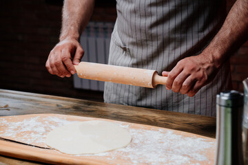 hands roll the dough into a thin layer. Cooking pizza, noodles or pitta at home