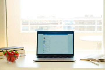 Fototapeta premium Home office concept. Designated work from home area near the window. Modern laptop, notebook and vase with flowers on table. Close up, copy space, background.