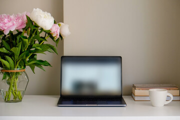 Home office concept. Designated work from home area near the window. Modern laptop, notebook and vase with flowers on table. Close up, copy space, background.