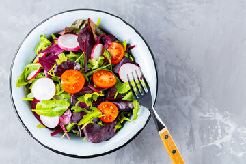 Salad with mix of greens on gray background. Healthy vegetable salad with cherry tomatoes, radish and mix salad. Copy space