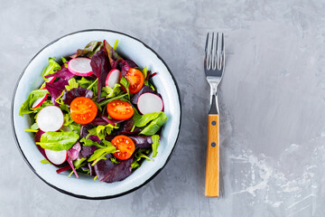 Salad with mix of greens on gray background. Healthy vegetable salad with cherry tomatoes, radish and mix salad. Copy space