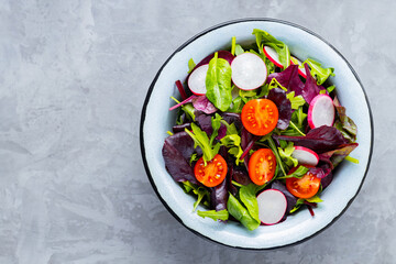 Salad with mix of greens on gray background. Healthy vegetable salad with cherry tomatoes, radish and mix salad. Copy space