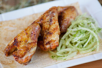 Pieces of fried poultry meat on pita bread, served with fresh vegetables on a plate and a wooden board.