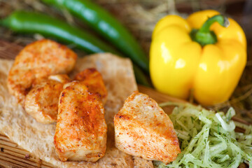 Pieces of grilled meat on pita bread, served with fresh peppers and salad on a wooden board and hay.