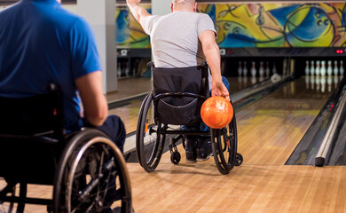 Two young disabled men in wheelchairs playing bowling in the club