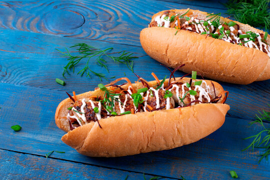 Sandwich with meatballs, grated orange and purple carrot, mustard and sour cream sauce in hot dog bun topped with herbs on the blue wooden table