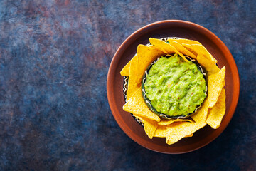 Traditional mexican sauce guacamole with tortilla chips in clay bowl. Bowl of guacamole with nachos chips on a dark background. Copy space. Top view