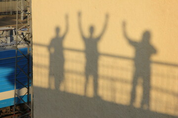 shadows of people created by the setting sun on the wall of a house near the railway station