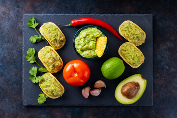 Guacamole sauce, nachos chips and ingredients on a dark background. Mexican guacamole sauce with...