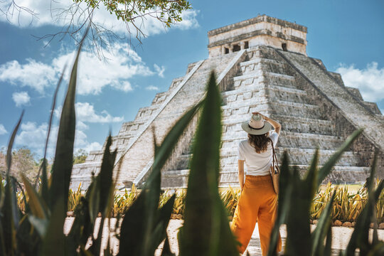 A young woman tourist in a hat stands against the background of the pyramid of Kukulcan in the ancient Mexican city of Chichen Itza. Travel concept.Mayan pyramids in Yucatan, Mexico